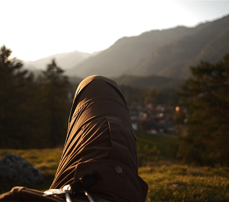 Eine Person liegt auf einer Wiese und blickt in die Berge bei Sonnenuntergang.