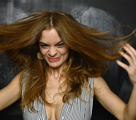 Patientin mit langen braunen Haaren schwingt schwungvoll ihre Haare und lächelt in die Kamera vor schwarzem Hintergrund