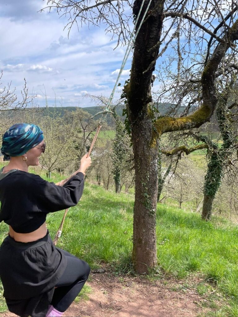 Patientin mit Kopftuch bei einer Wanderung in hügeliger Landschaft mit Wald und Wiesen